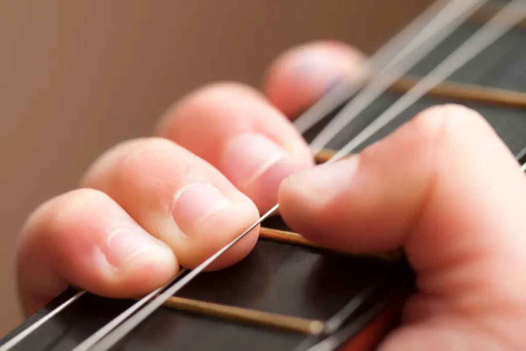 Doigts appuyant sur les cordes d’une guitare ils illustrent une des différences entre ukulélé et guitare