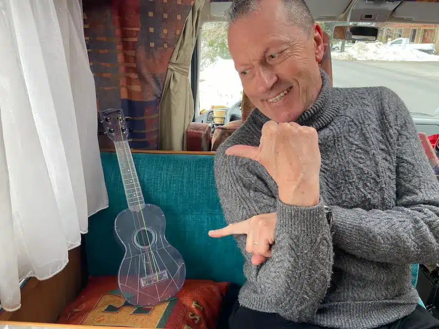 Denis montre son ukulélé sur un canapé de camping car pou progresser plus rapidement au ukulélé